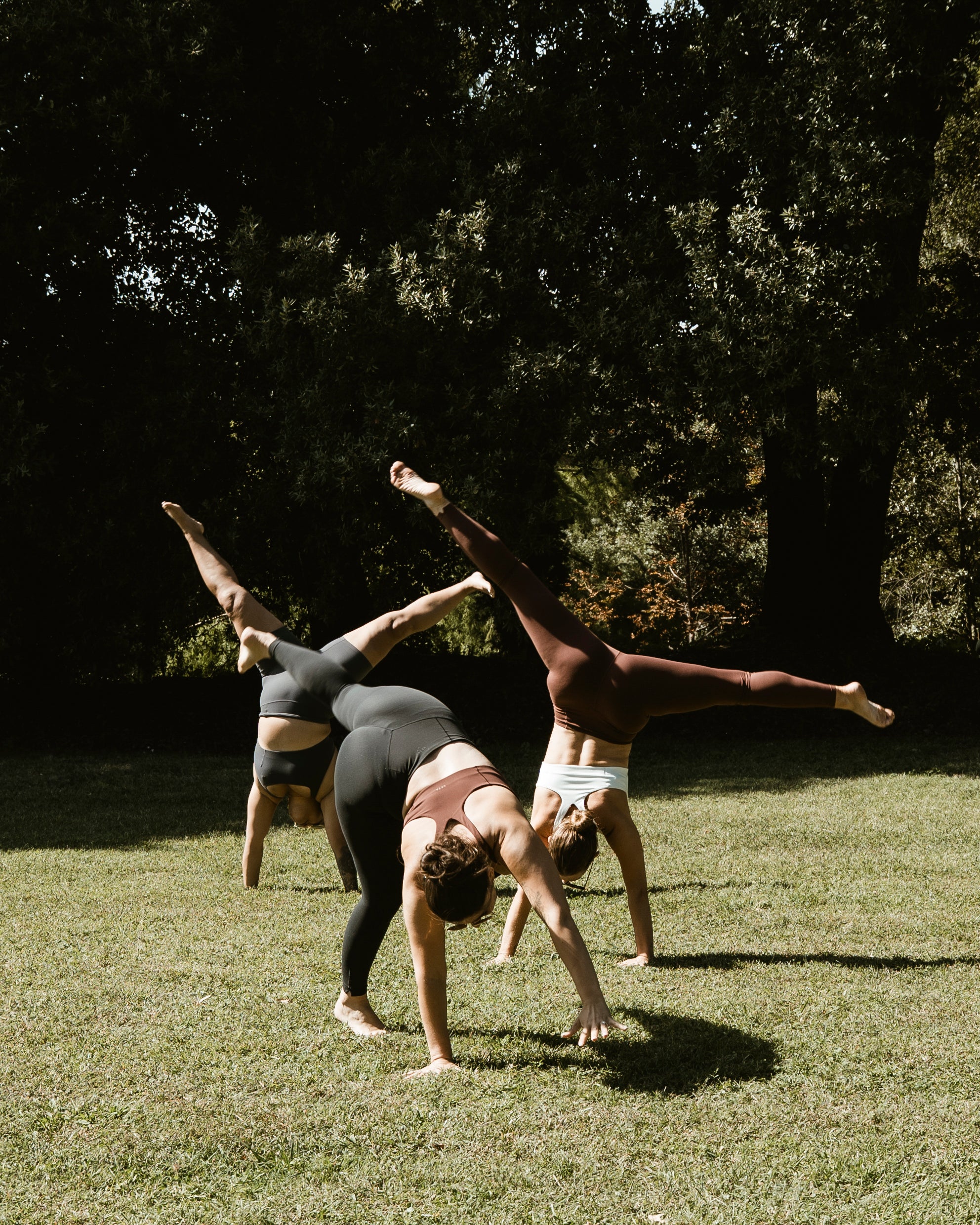 Three people in VETA apparel cartwheeling on a sunlit lawn.